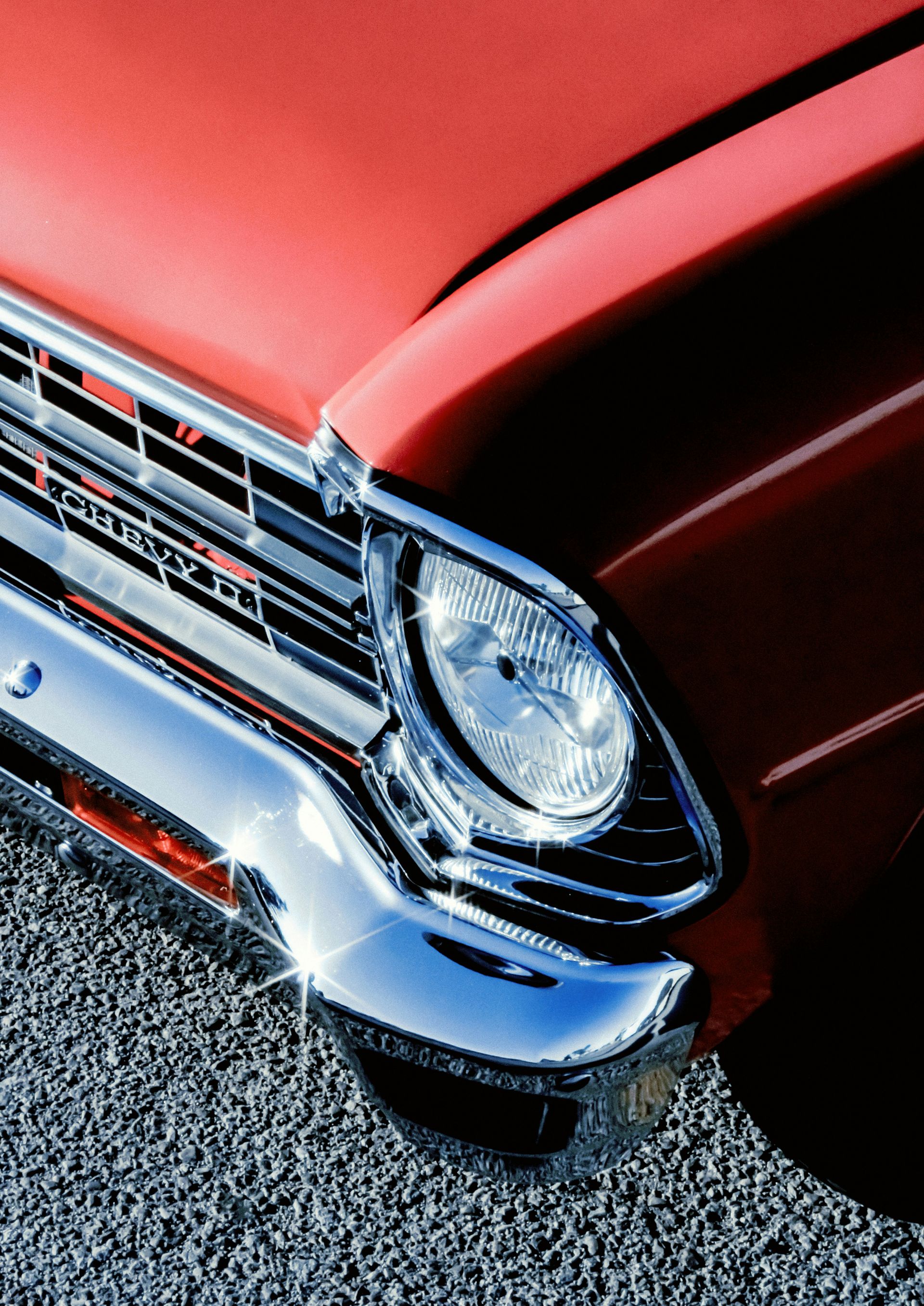 Red classic car's shiny chrome bumper and headlight.