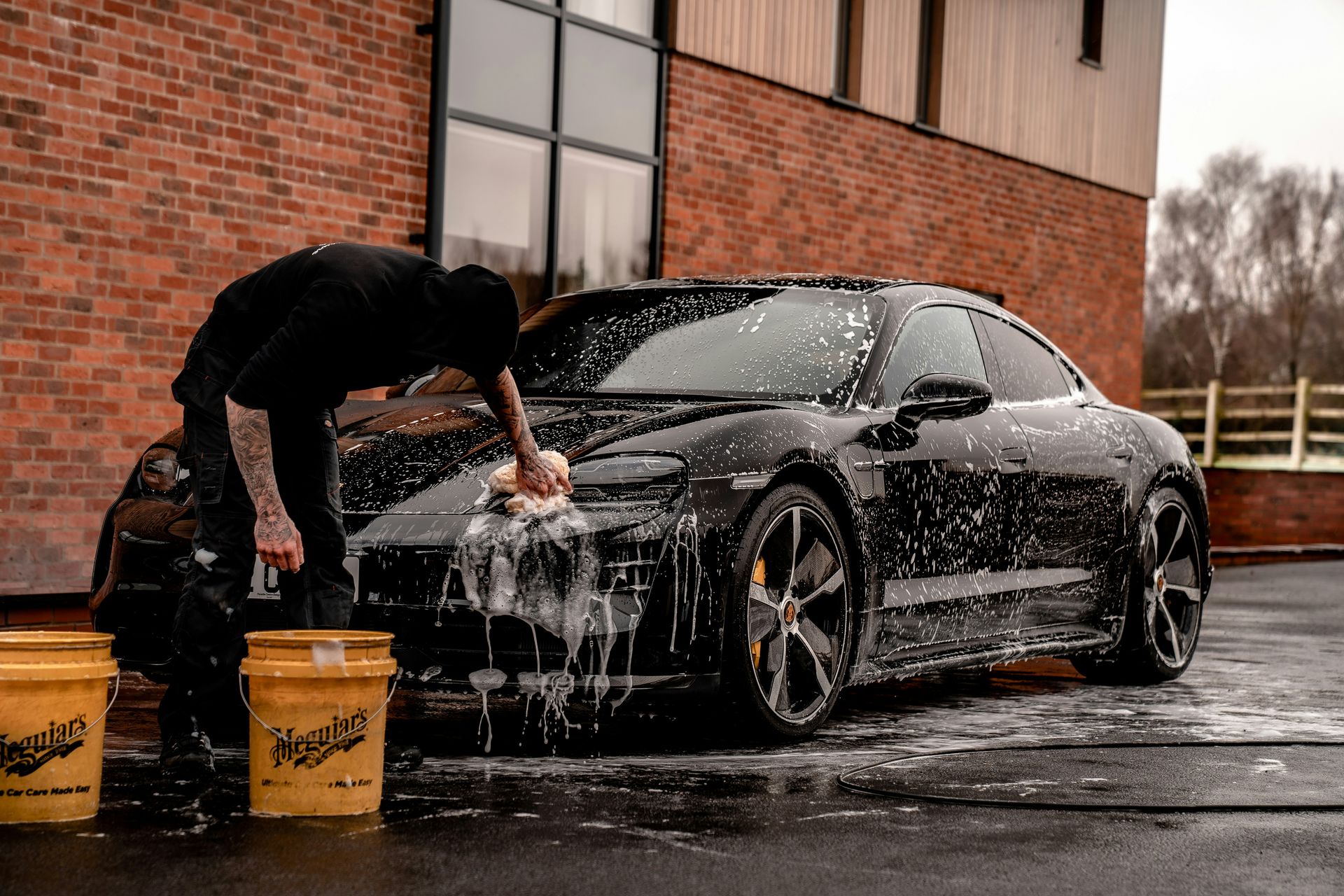 man in black t-shirt and black pants doing water splash on black coupe during daytime