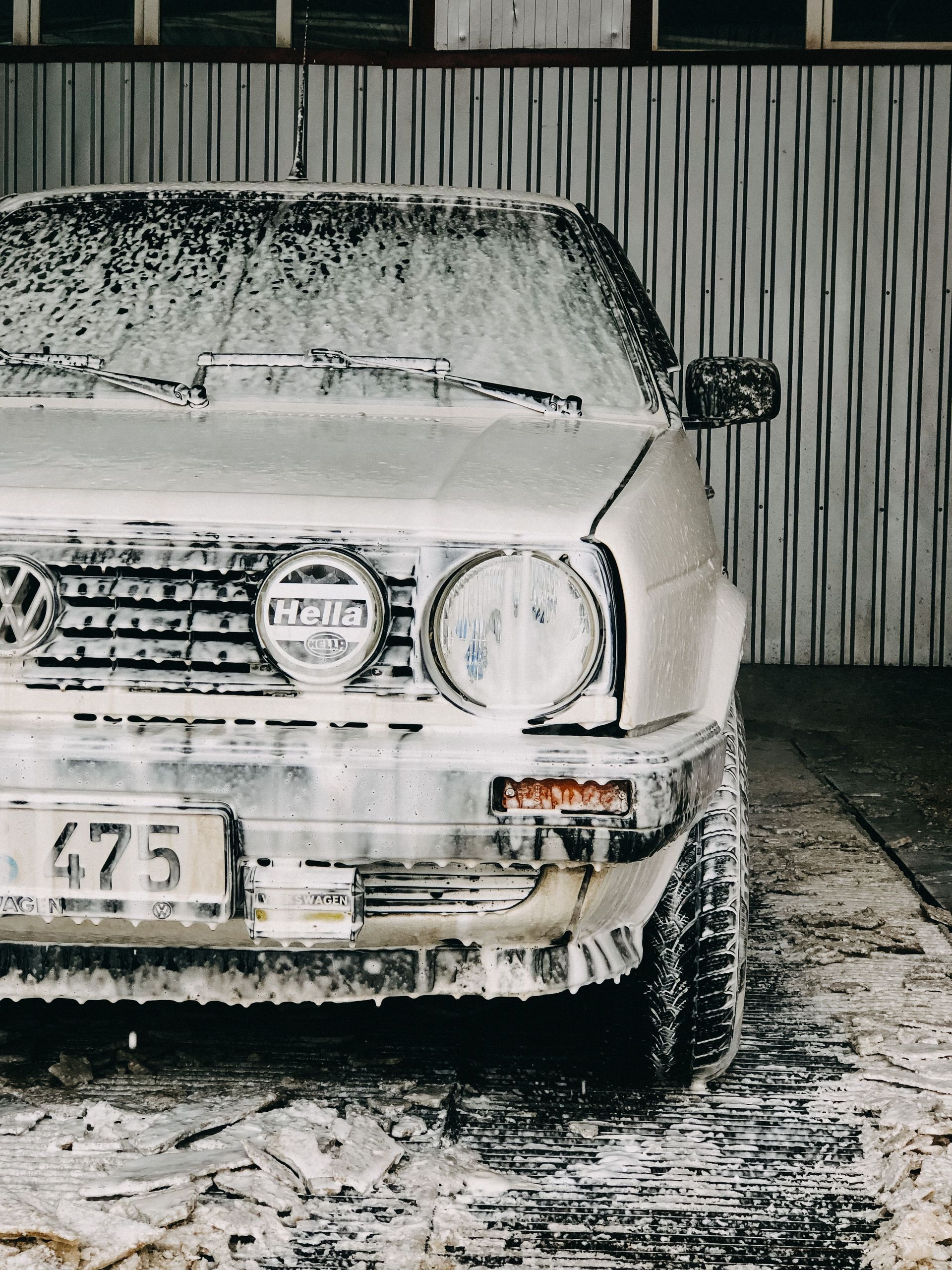 Close-up of a classic Volks-wagen covered in soap foam during a car wash in a garage.